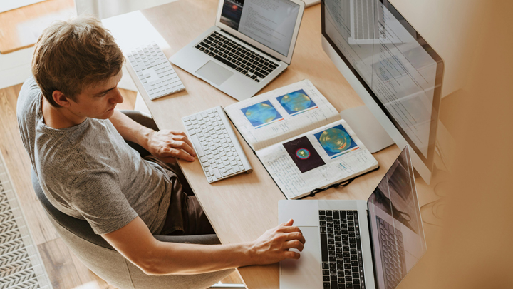 Man working at desk with two laptops and monitor