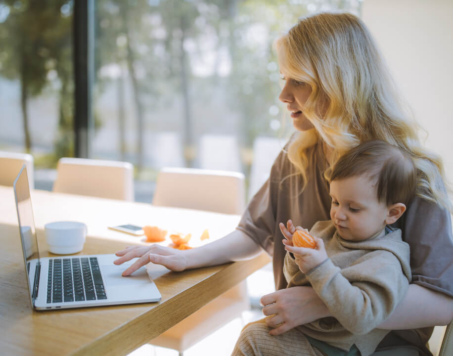 Woman holding a child on her lap whilst working on a laptop