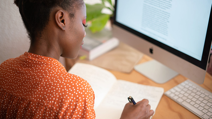 woman writing in book in front of computer