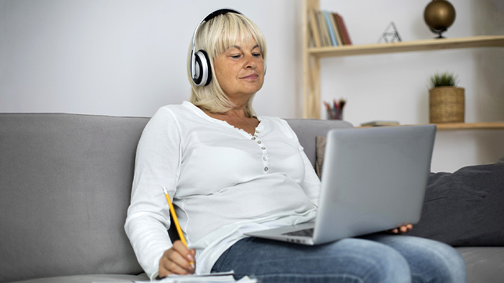 woman sat on sofa with headphones on, working at laptop