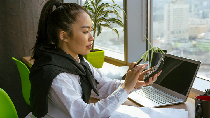 Woman working at laptop, using her mobile phone